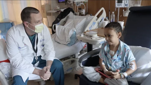 Douglas Overbey, MD, an assistant professor in the department of surgery at Duke University School of Medicine, checks in with 9-year-old Kensley Frizzell as she recovers from heart surgery. Image courtesy of Duke Health and Duke University School of Medicine.